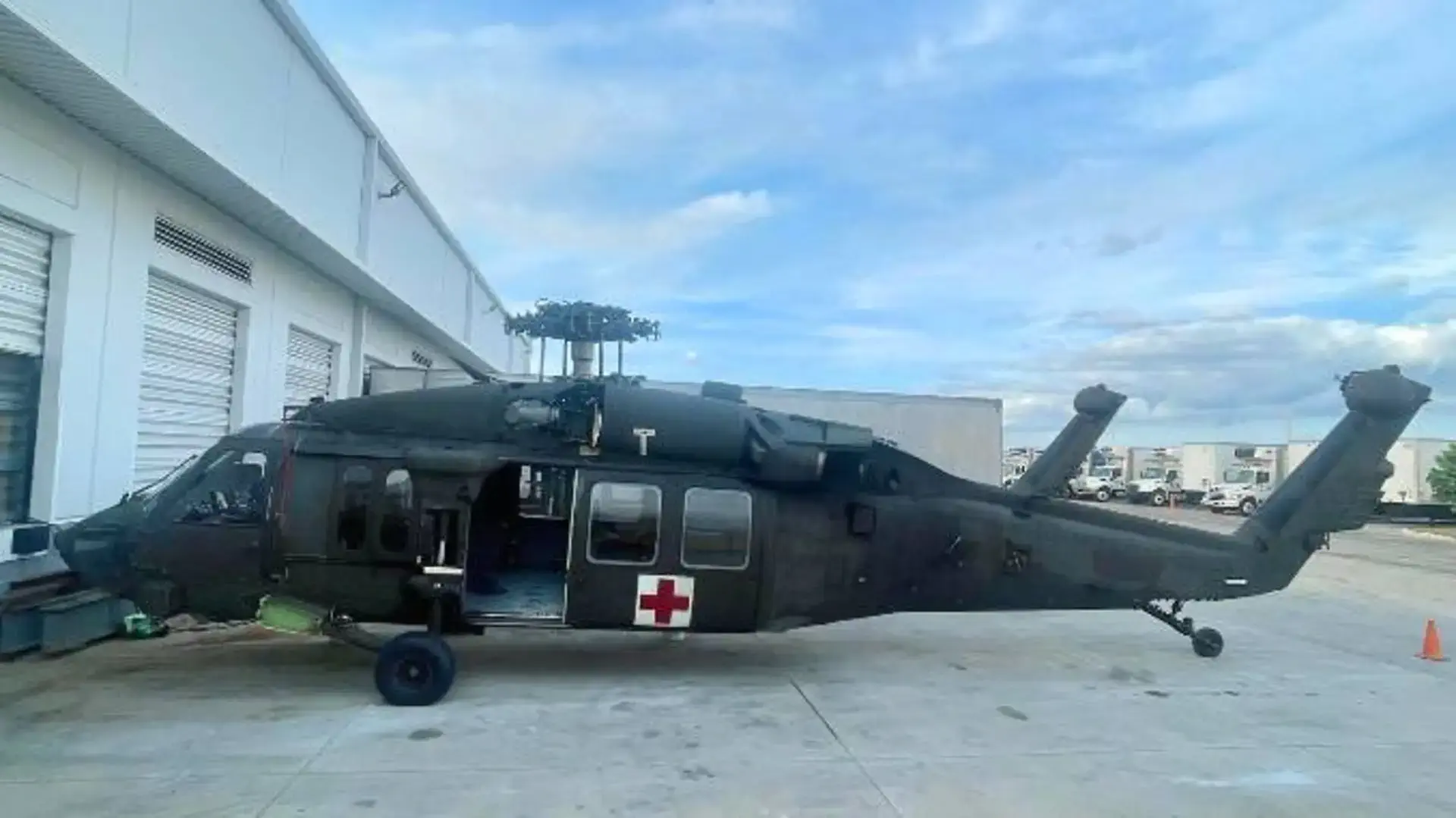 Black military helicopter with a red cross symbol parked on a concrete surface near a building.